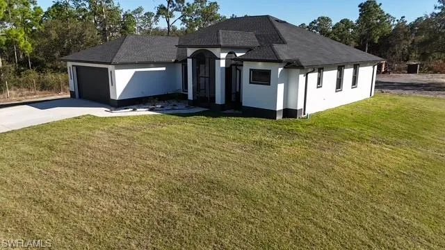 View of front facade with a front lawn, stucco siding, an attached garage, and driveway