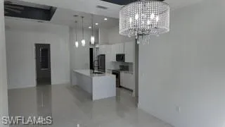 Kitchen featuring white cabinetry, black range oven, an island with sink, hanging lights, and light tile patterned flooring