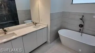 Bathroom featuring a soaking tub, double vanity, and tile walls