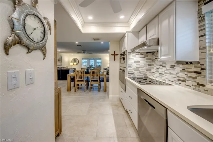 Kitchen with ceiling fan, stainless steel appliances, white cabinets, decorative backsplash, and wall chimney exhaust hood