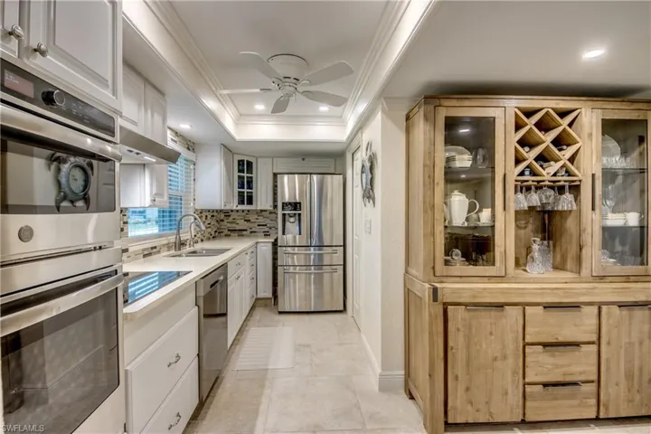 Kitchen with appliances with stainless steel finishes, tasteful backsplash, sink, ceiling fan, and a raised ceiling