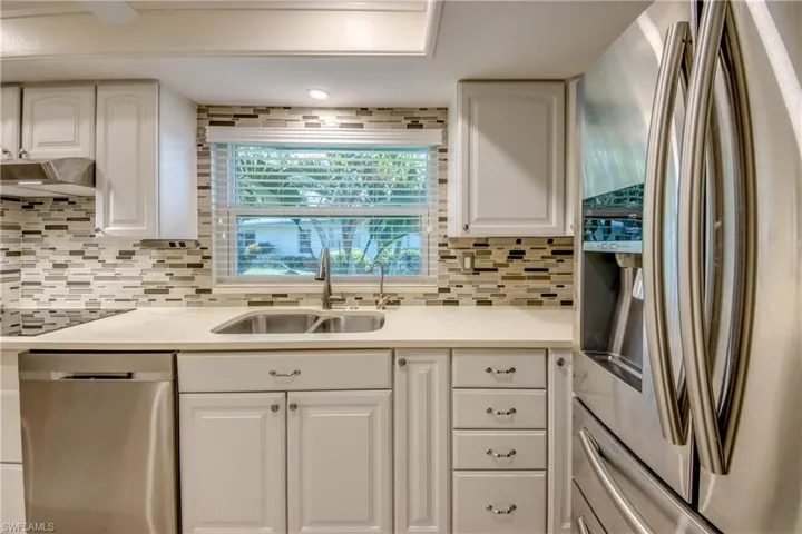Kitchen with white cabinetry, stainless steel appliances, wall chimney exhaust hood, sink, and backsplash