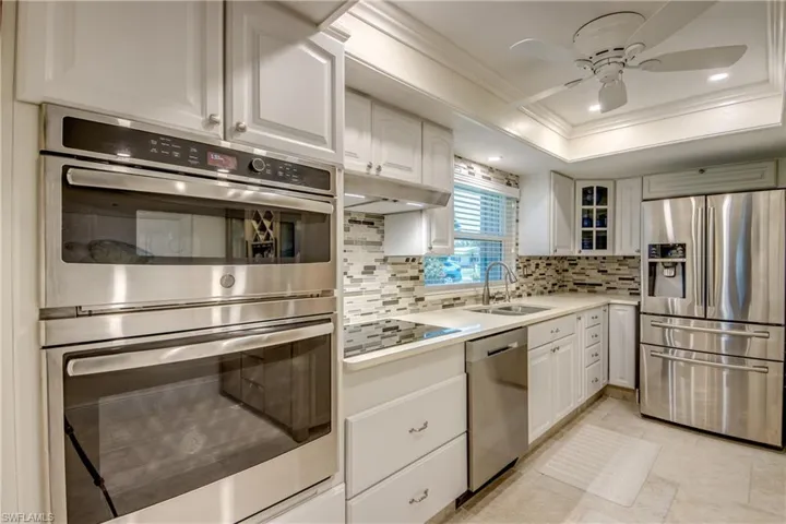 Kitchen featuring a tray ceiling, white cabinets, sink, appliances with stainless steel finishes, and backsplash