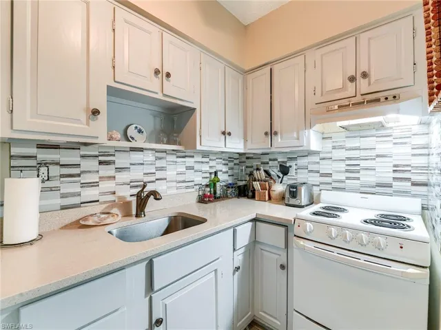 Kitchen with electric range, light stone counters, white cabinets, and tasteful backsplash
