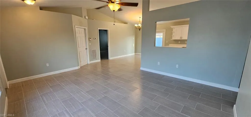 Empty room with ceiling fan, lofted ceiling, and a chandelier