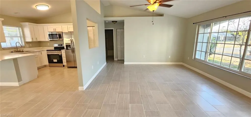 Kitchen with light countertops, stainless steel appliances, white cabinets, ceiling fan, and vaulted ceiling