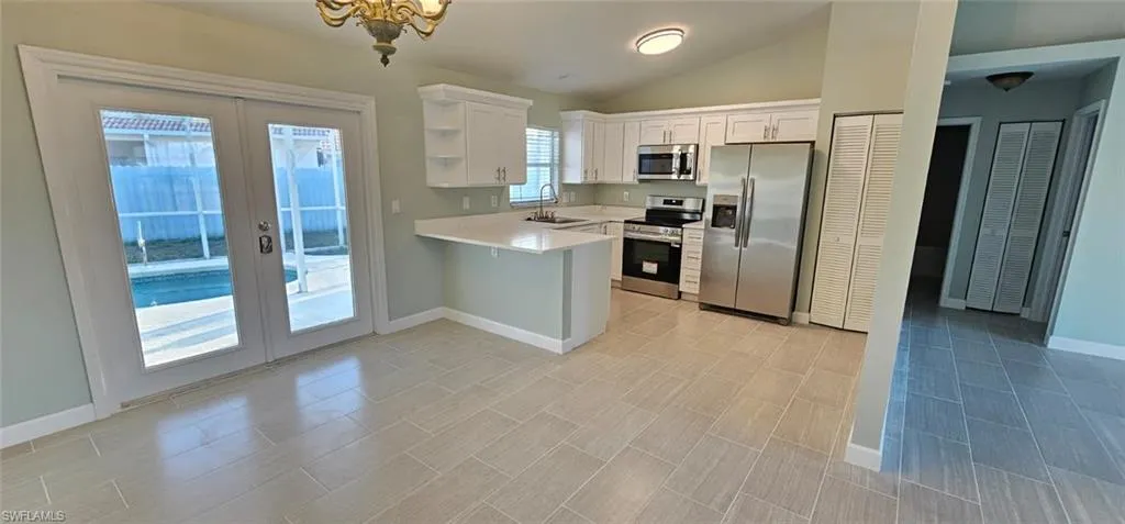 Kitchen featuring stainless steel appliances, vaulted ceiling, white cabinetry, french doors, and a peninsula