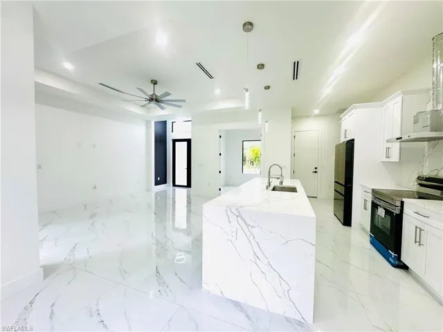 Kitchen featuring a ceiling fan, electric range, white cabinets, light stone counters, and a tray ceiling