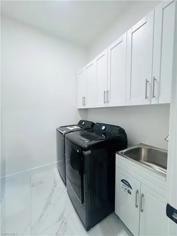 Laundry room with cabinet space, washing machine and dryer, and light marble finish flooring