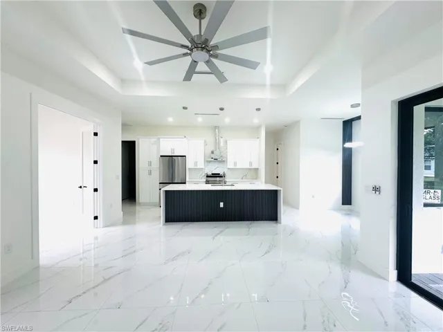Kitchen with open floor plan, white cabinetry, an island with sink, a ceiling fan, and a raised ceiling
