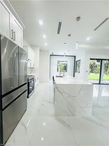 Kitchen featuring stainless steel appliances, white cabinets, light stone countertops, and an island with sink