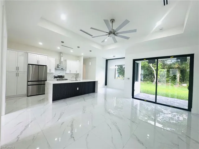 Kitchen featuring a raised ceiling, stainless steel appliances, white cabinetry, open floor plan, and backsplash