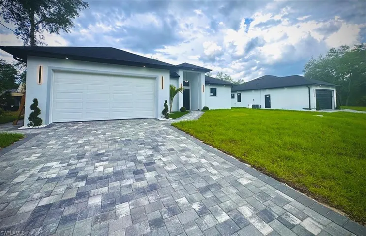 View of front of property featuring an attached garage, a front yard, decorative driveway, and stucco siding
