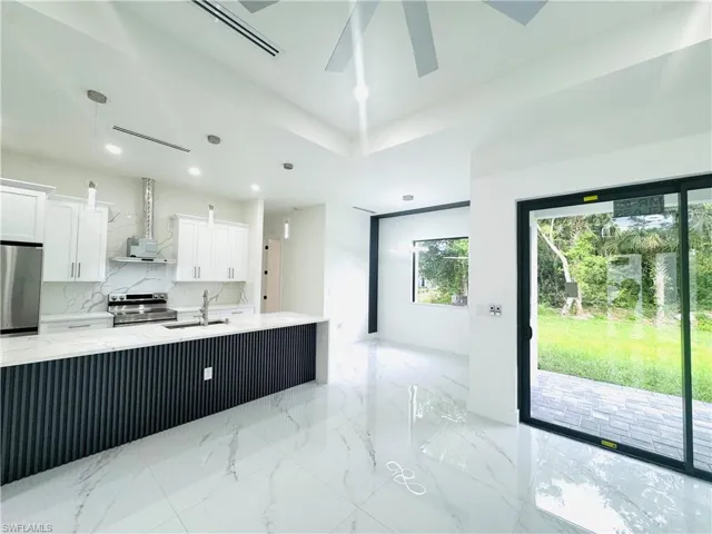 Kitchen featuring white cabinetry, light stone counters, stainless steel appliances, and decorative light fixtures