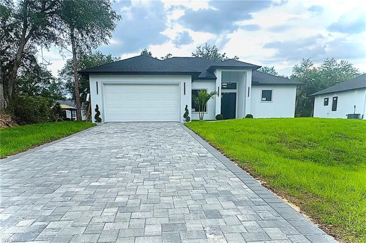 View of front of house with an attached garage, a front lawn, decorative driveway, and stucco siding