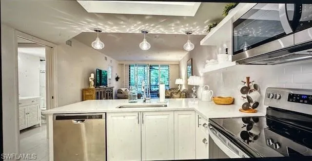 Kitchen with stainless steel appliances, a peninsula, white cabinets, and hanging light fixtures