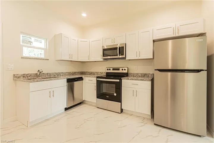 Kitchen with light tile patterned flooring, sink, stainless steel appliances, and white cabinets