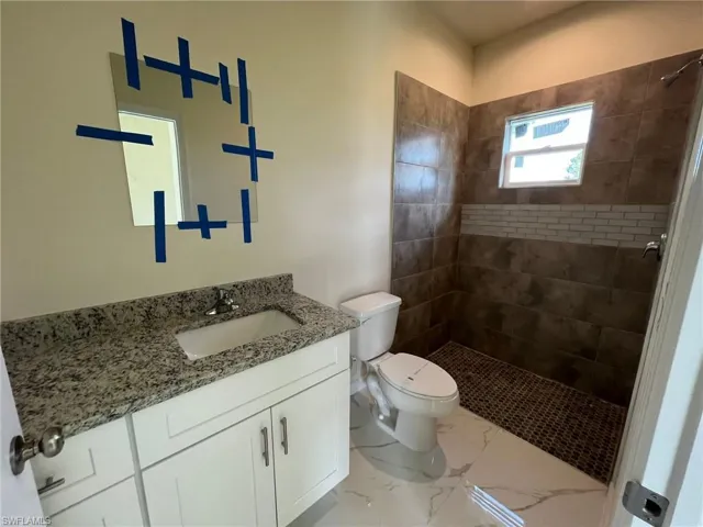 Bathroom featuring tile patterned floors, vanity, toilet, and tiled shower