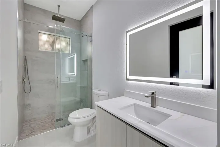 Full bath with vanity, a textured wall, a marble finish shower, and light tile patterned floors