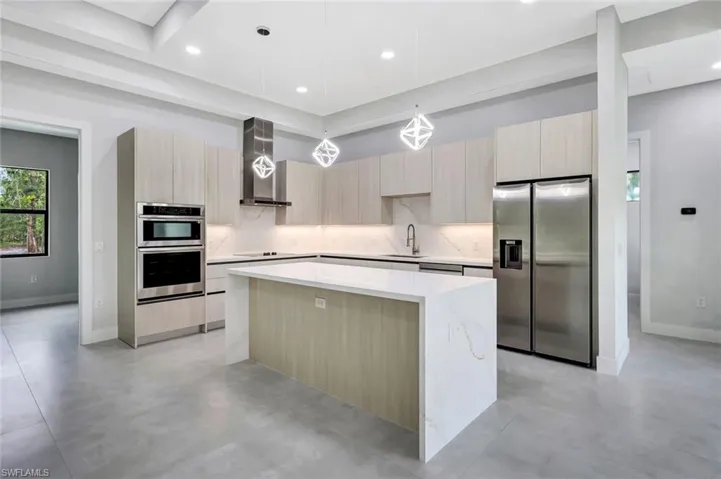Kitchen featuring light brown cabinets, appliances with stainless steel finishes, a center island, hanging light fixtures, and light stone counters