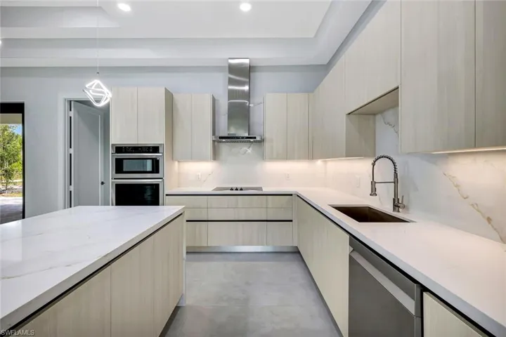 Kitchen featuring light brown cabinets, light stone countertops, hanging light fixtures, stainless steel appliances, and decorative backsplash