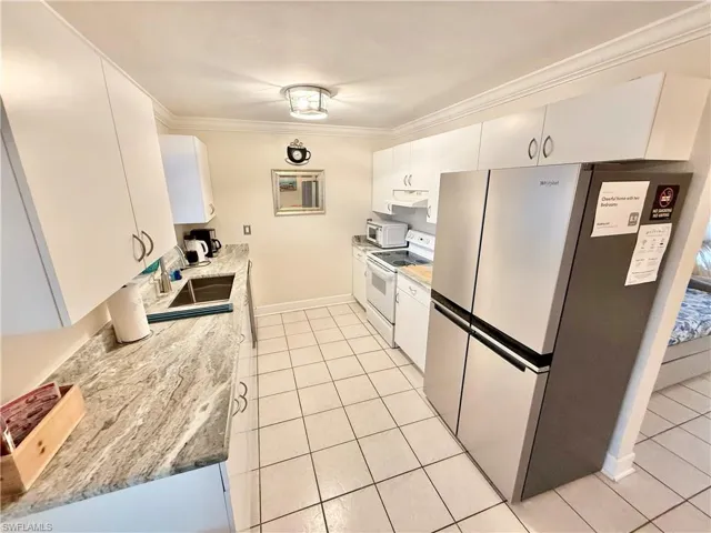 Kitchen featuring white appliances, crown molding, light tile patterned floors, white cabinetry, and baseboards