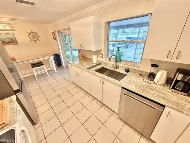 Kitchen with stainless steel dishwasher, light tile patterned floors, white cabinetry, ornamental molding, and a sink