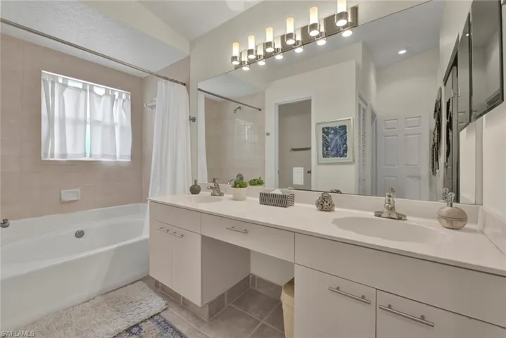Bathroom featuring double vanity, shower / tub combo, and light tile patterned flooring