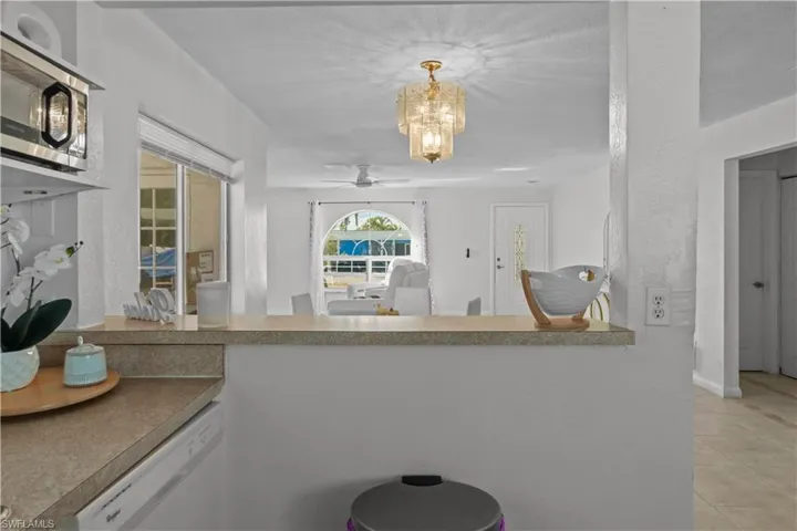 Kitchen with stainless steel microwave, dishwasher, a ceiling fan, hanging lights, and light countertops