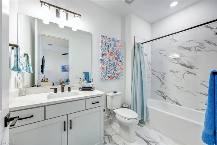 Bathroom featuring shower / bath combo, vanity, light marble finish floors, and recessed lighting