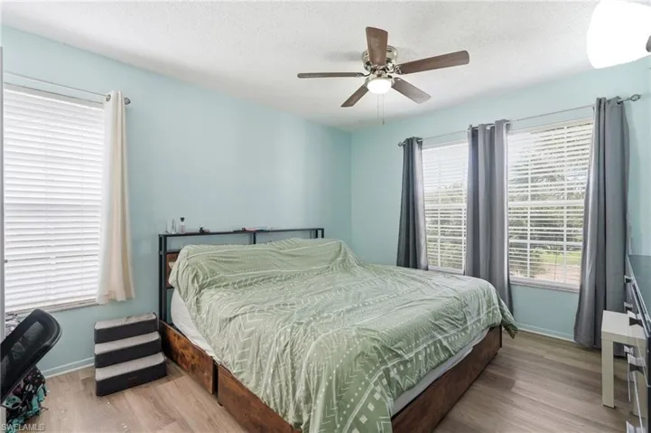 Bedroom featuring multiple windows with blinds, a ceiling fan with integrated lighting, and wood-finish flooring