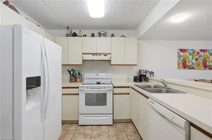 Kitchen featuring white appliances, cream cabinetry, light-toned countertops, and tile flooring