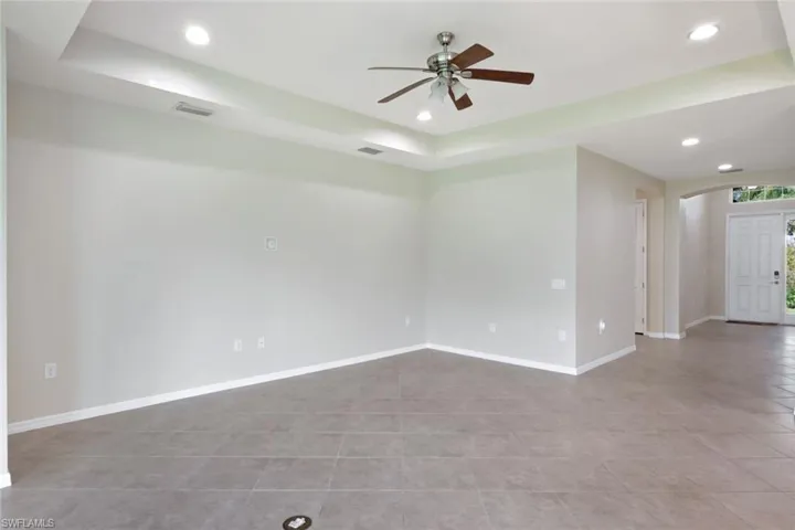 Tray ceiling with recessed lighting, ceiling fan, tile flooring, and a paneled entry door with transom window