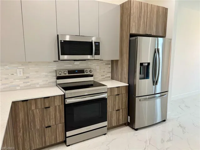 Kitchen featuring backsplash, appliances with stainless steel finishes, and light tile flooring