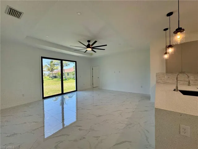 Tiled empty room with sink, ceiling fan, and a tray ceiling