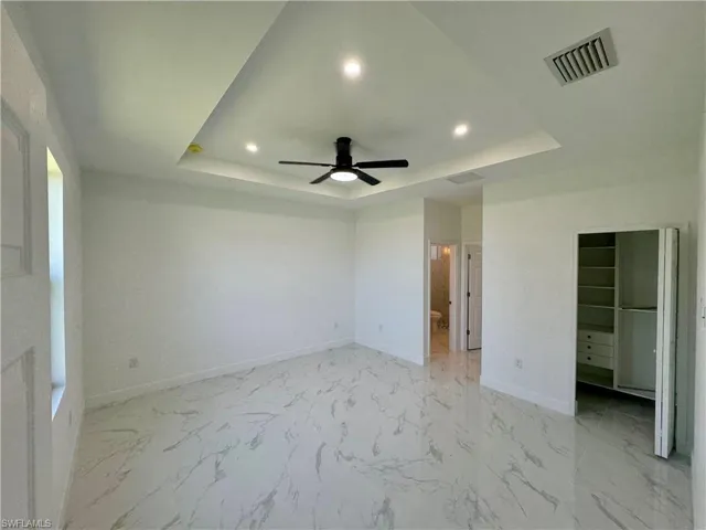 Unfurnished bedroom with a closet, ceiling fan, a tray ceiling, and light tile flooring