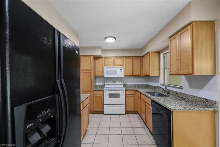 Kitchen with light stone counters, black appliances, sink, and light tile floors