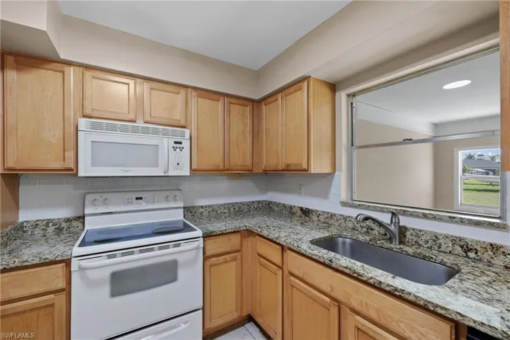 Kitchen featuring light stone countertops, sink, white appliances, and backsplash