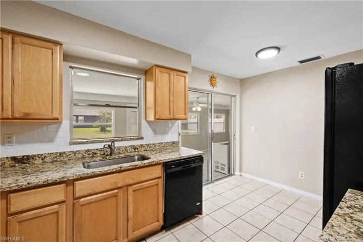 Kitchen with backsplash, sink, black appliances, and light tile floors