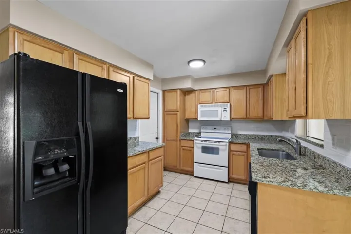 Kitchen featuring white appliances, light stone countertops, sink, and light tile floors