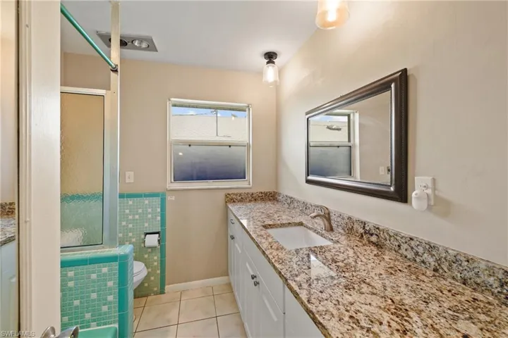 Bathroom with tile flooring, vanity with extensive cabinet space, toilet, and tile walls