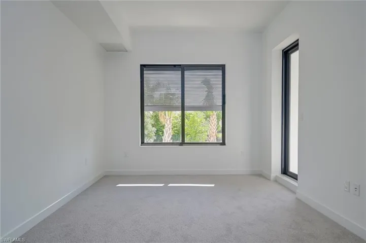 2nd bedroom with access to balcony area - overlooks greenery and has large palms outside window