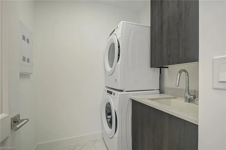 laundry room with sink and cabinets, washer & dryer stacks