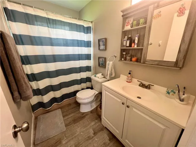 Bathroom with vanity, toilet, curtained shower, and LVP  wood-type flooring