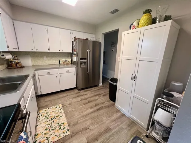 Kitchen featuring range, light LVP wood-style flooring, stainless steel fridge with ice dispenser, tasteful backsplash, and white cabinets