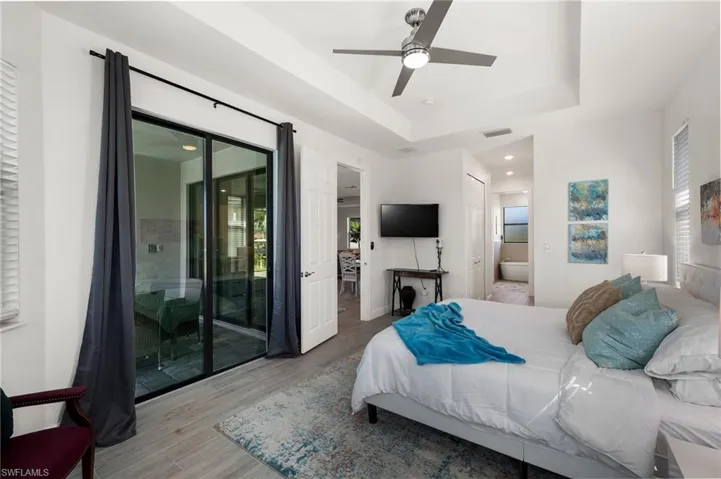 Bedroom with ensuite bath, visible vents, access to exterior, a raised ceiling, and wood finished floors