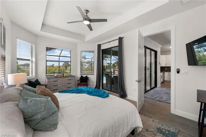 Bedroom featuring baseboards, ceiling fan, a tray ceiling, wood finished floors, and access to outside