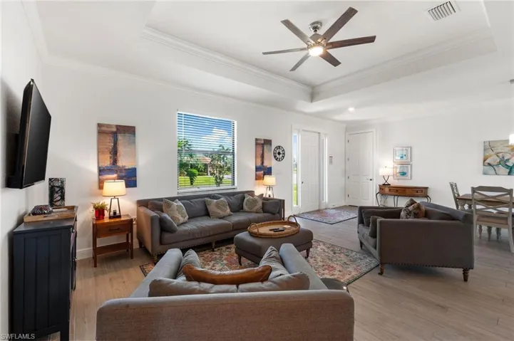 Living area featuring a tray ceiling, light wood-type flooring, and visible vents
