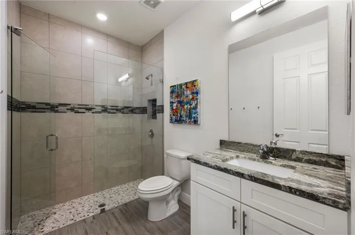 Bathroom with visible vents, toilet, a shower stall, vanity, and wood finished floors