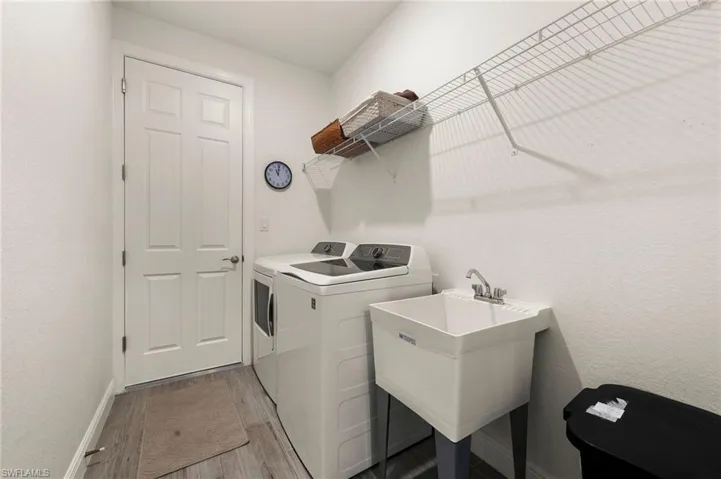 Laundry room with laundry area, light wood-type flooring, a sink, washer and dryer, and baseboards